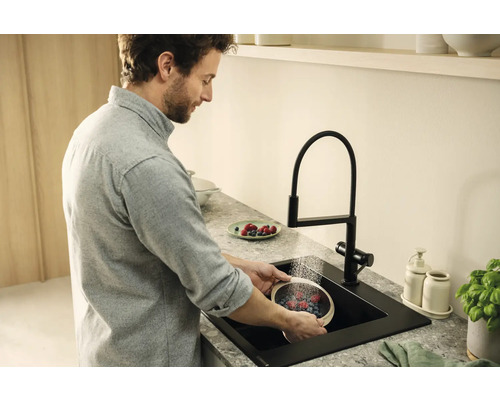 Muž myje bobule v černém kuchyňském dřezu s baterií.