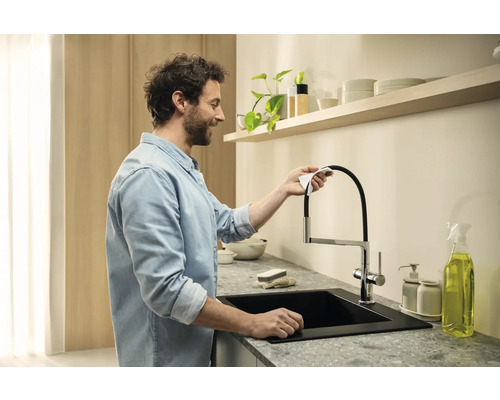 Muž čistí kuchyňskou baterii s černým dřezem a pracovní deskou