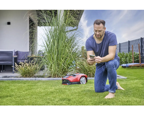 Muž ovládá robotickou sekačku na trávu pomocí smartphonu na zahradě