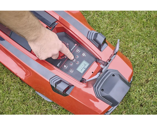 Ruka ovládá ovládací panel robotické sekačky na trávníku.