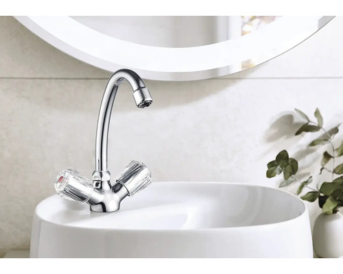 Lesklá vodovodní baterie s transparentními rukojeťmi na bílém umyvadle