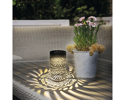 Dekorativní stolní lampa s listovým vzorem vedle květináče na zahradním stole