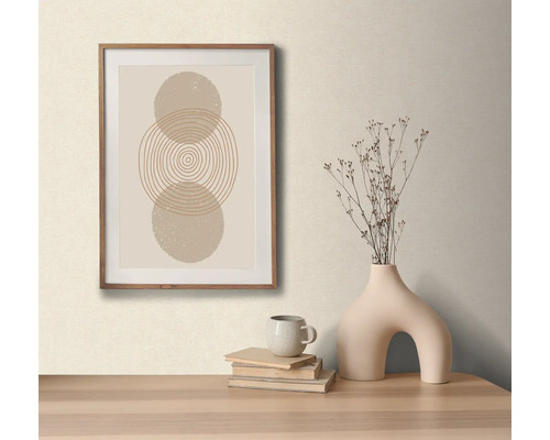 Dekorativní aranžmá s zarámovaným obrazem s abstraktním kruhovým motivem, váza se suchými květinami, šálek a knihy na stole.