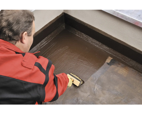 Řemeslník nanáší štětcem hydroizolaci na podlahu