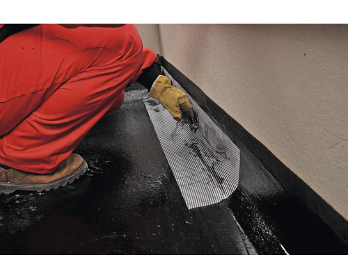 Osoba nanáší těsnicí tkaninu na podlahu.