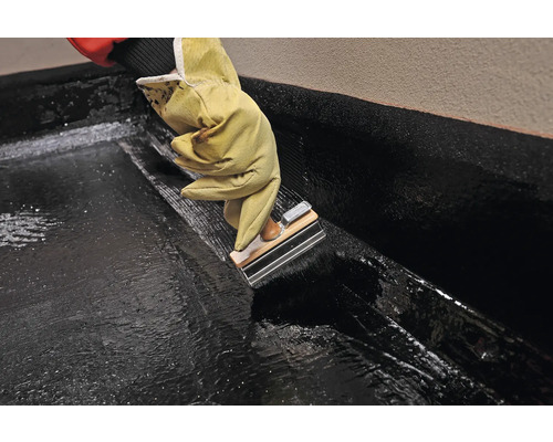 Osoba v rukavicích nanáší bitumenový tmel pomocí hladítka