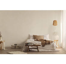 Světlá ložnice s postelí, dekou, polštáři, odkládacím stolkem, lampou a dekorativními prvky pro přátelskou atmosféru.