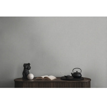 Dekorativní zátiší s čajovou konvicí, knihou a sochou na dřevěné skříňce před jednobarevnou stěnou.