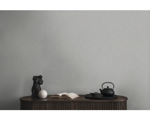 Dekorativní zátiší s čajovou konvicí, knihou a sochou na dřevěné skříňce před jednobarevnou stěnou.