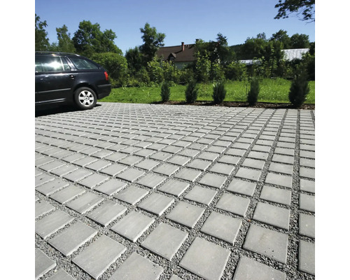 Dlažební kostky na příjezdové cestě s autem v pozadí.