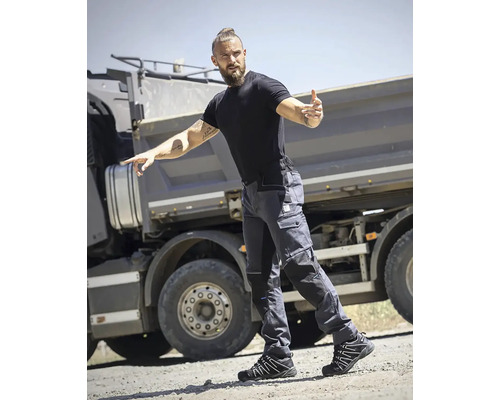 Muž má na sobě pracovní kalhoty, tričko a bezpečnostní obuv před nákladním autem.