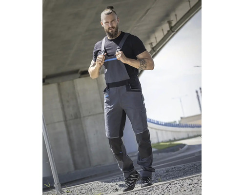 Muž má na sobě šedé pracovní kalhoty a černé tričko pod mostem.