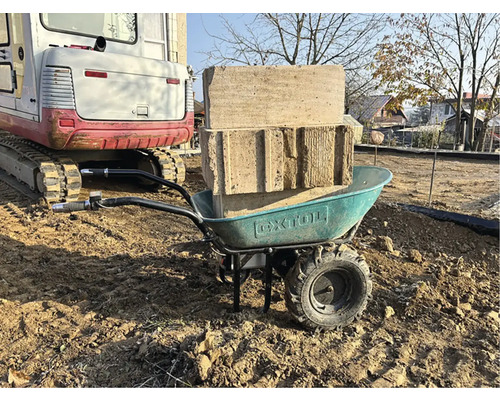 Kolečko s kameny a pískem na pozemku, v pozadí bagr.