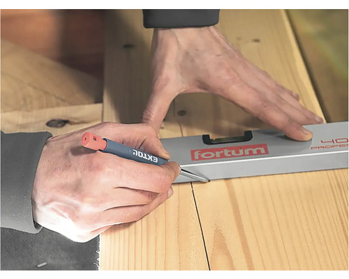 Osoba kreslí tesařskou tužkou čáru na dřevěné desce pomocí vodováhy.