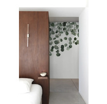 Ložnice s dřevěnou stěnou, nástěnnou lampou, malou policí a nástěnnou malbou s motivy eukalyptu.