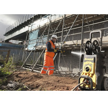 Stavební dělník čistí cihlovou zeď na staveništi žlutým tlakovým čističem.