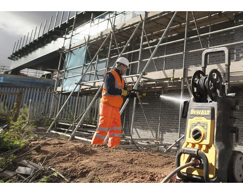 Stavební dělník čistí cihlovou zeď na staveništi žlutým tlakovým čističem.