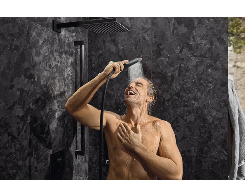 Muž ve sprše s hlavovou a ruční sprchou v koupelně s tmavými obklady