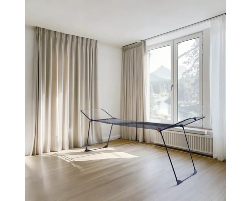 Kovový sušák na prádlo v světlé místnosti s oknem a závěsy