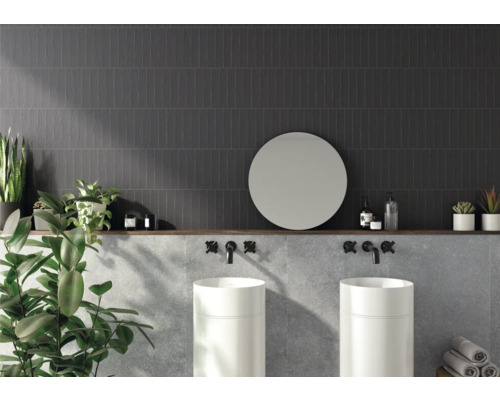 Koupelna s tmavými obkládačkami, dvěma umyvadly, kulatým zrcadlem a dekorací