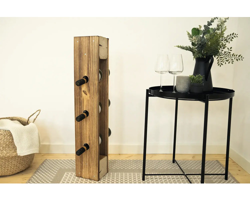 Dřevěný stojan na víno s plnými lahvemi vína vedle stolu s dekorací ve světlé místnosti.