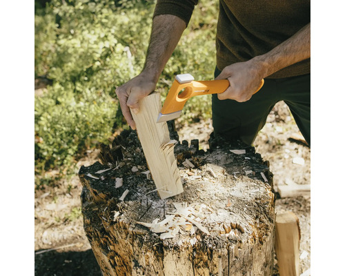 Osoba štípe dříví štípací sekerou na špalku.