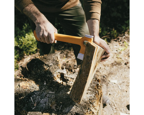 Osoba štípe dříví štípací sekerou na špalku.