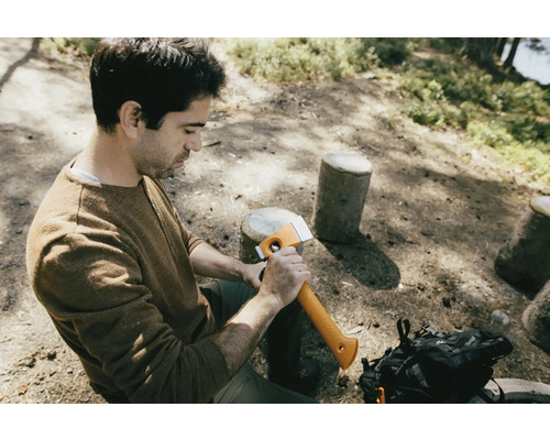 Muž sedí v lese a drží sekeru.