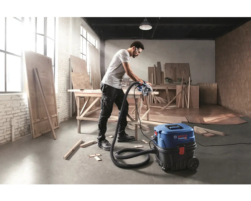 Muž řeže prkno kotoučovou pilou, která je připojena k vysavači Bosch, v dílně.