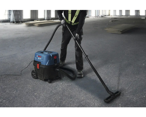 Muž používá průmyslový vysavač Bosch k úklidu hrubé stavby.