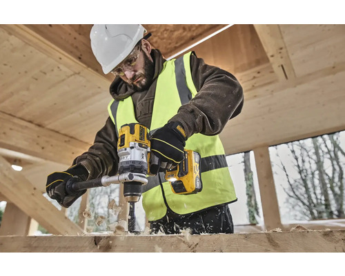 Stavební dělník vrtá žlutou akumulátorovou vrtačkou DeWalt díru do dřevěné desky.