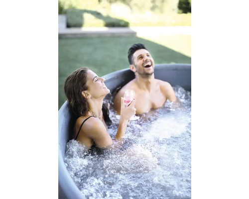 Dva lidé se smějí a relaxují v koupací kádi na zahradě.