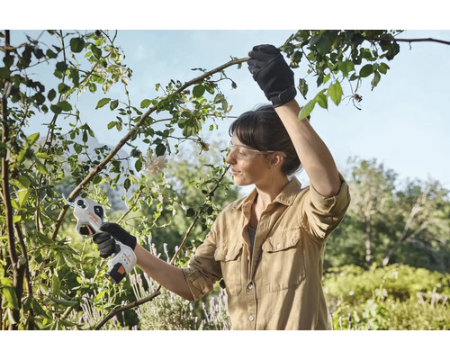 Žena používá akumulátorové zahradní nůžky ke stříhání větví v zahradě.
