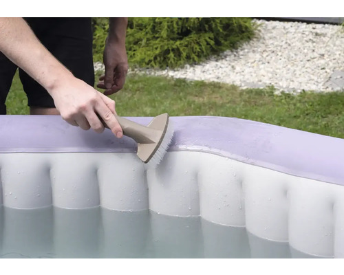 Osoba čistí nafukovací bazén kartáčem.