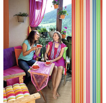 Dvě ženy pijí kávu na balkóně s barevnou výzdobou a lamelovým závěsem.