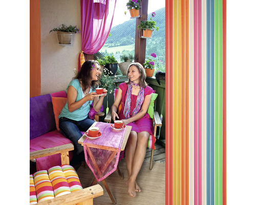 Dvě ženy pijí kávu na balkóně s barevnou výzdobou a lamelovým závěsem.