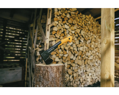 Štípací sekera na špalku před hromadou dřeva