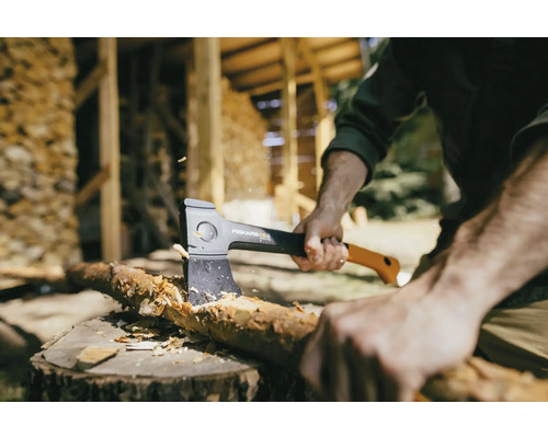 Muž štípe dřevo sekerou Fiskars na pařezu.