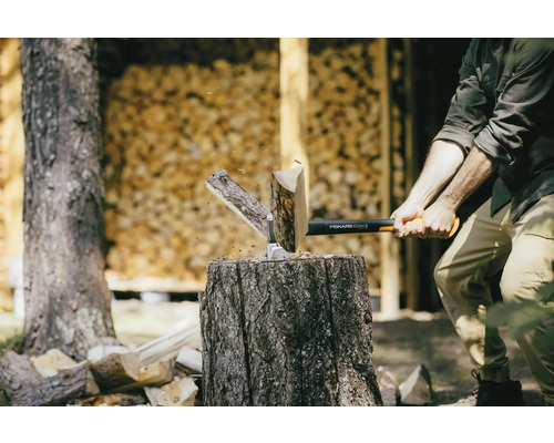 Muž štípe dřevo se sekerou Fiskars na špalku