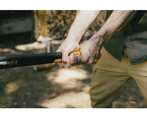 Osoba drží štípací sekeru Fiskars na štípání dřeva.