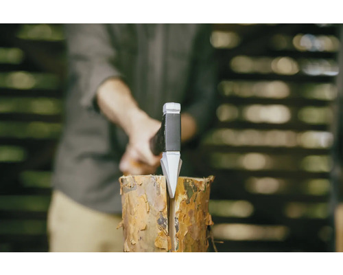 Muž štípe špalek dřeva štípací sekerou.