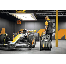 Muž s kufříkem na nářadí DeWalt vedle závodního auta v garáži