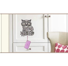 Dekorativní nástěnný háček s motivem sovy na bílých dveřích skříně s mobilním telefonem.