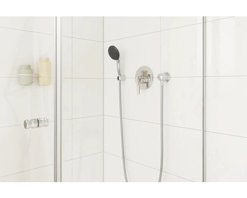 Moderní sprchový kout s baterií a ruční sprchou na bílém dlaždicovém pozadí.