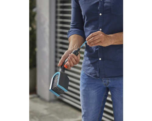 Osoba plní kartáč čisticí tyčí pro zavlažování zahrady.