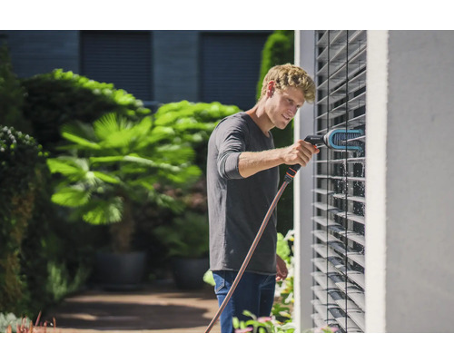 Muž čistí žaluzie kartáčem a vodní hadicí na zahradě.