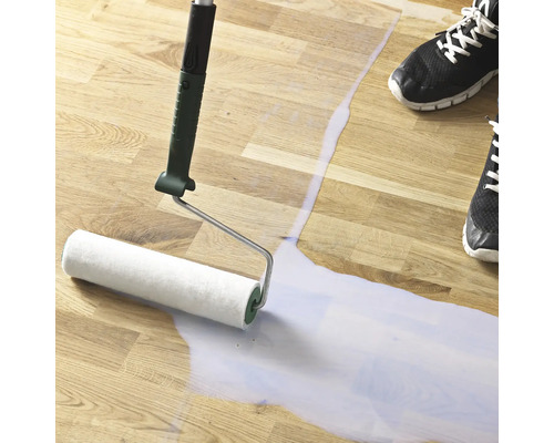 Nátěr se nanáší válečkem na dřevěnou podlahu.