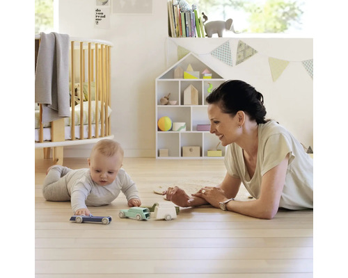 Matka a dítě si hrají s autíčky ze dřeva na podlaze v prosvětleném dětském pokoji s postýlkou a policí