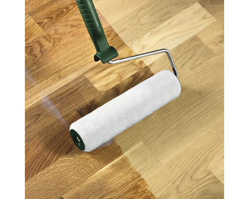 Váleček na barvu nanáší barvu na dřevěnou podlahu.