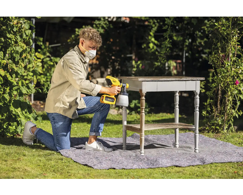 Muž používá venku stříkací pistoli k lakování stolu.